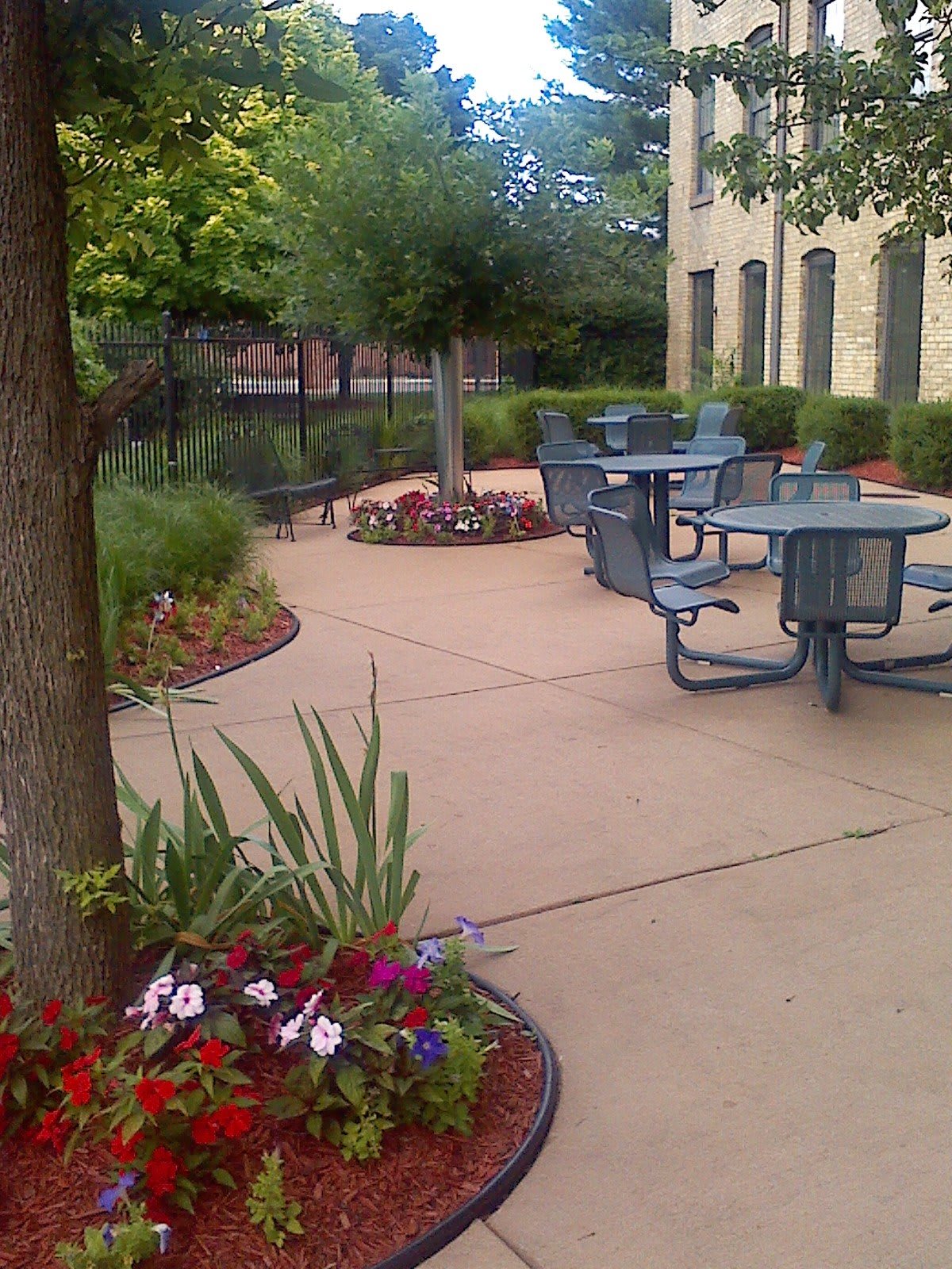 A peaceful outdoor patio area with tables and chairs surrounded by lush greenery and flowers.