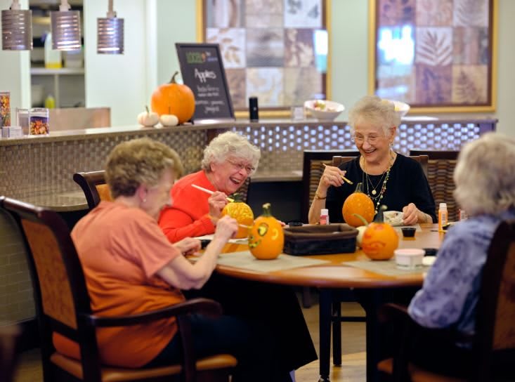 A group of seniors engaged in pumpkin decorating activities indoors.
