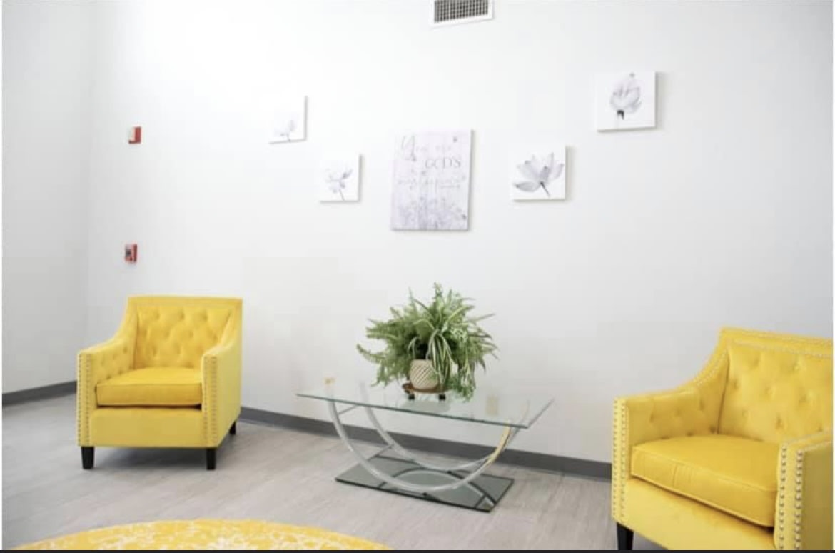 A modern living room with bright yellow chairs and a glass coffee table, featuring minimalist wall art and an indoor plant.