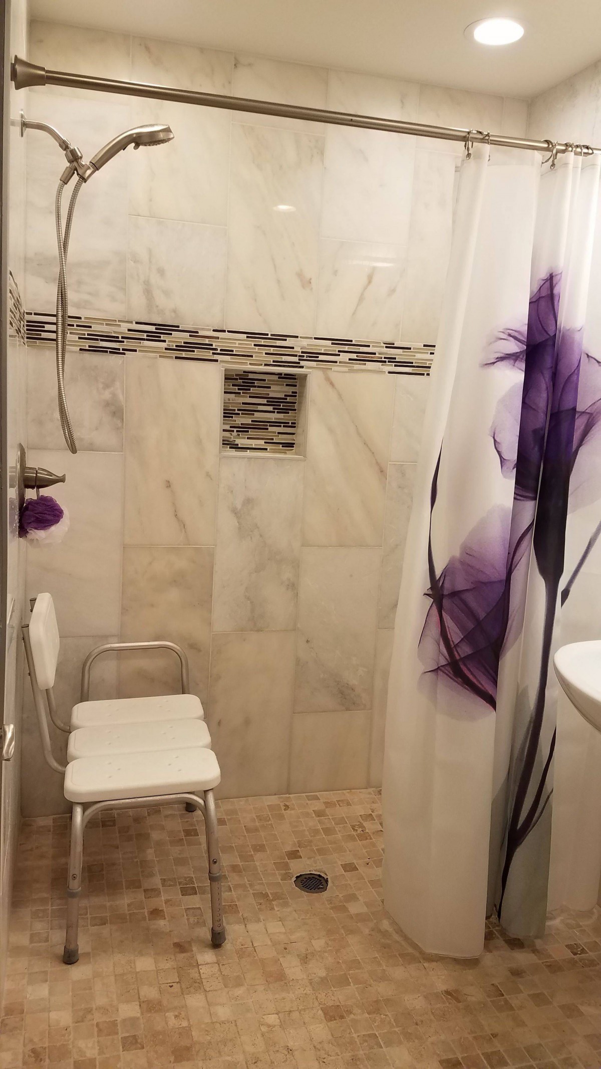 A bathroom shower area with a marble tiled wall and a chair, featuring a decorative purple shower curtain.