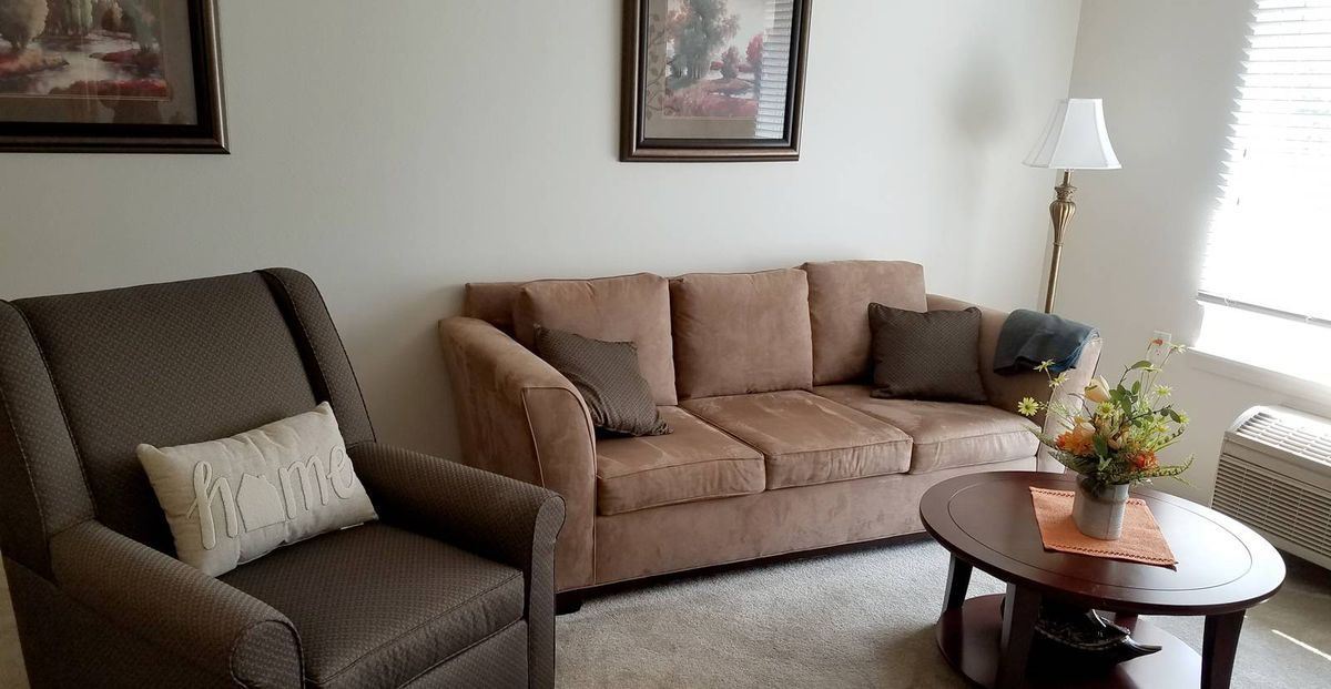 A cozy living room featuring a beige sofa with cushions, an armchair, and a wooden coffee table beneath a decorative painting.