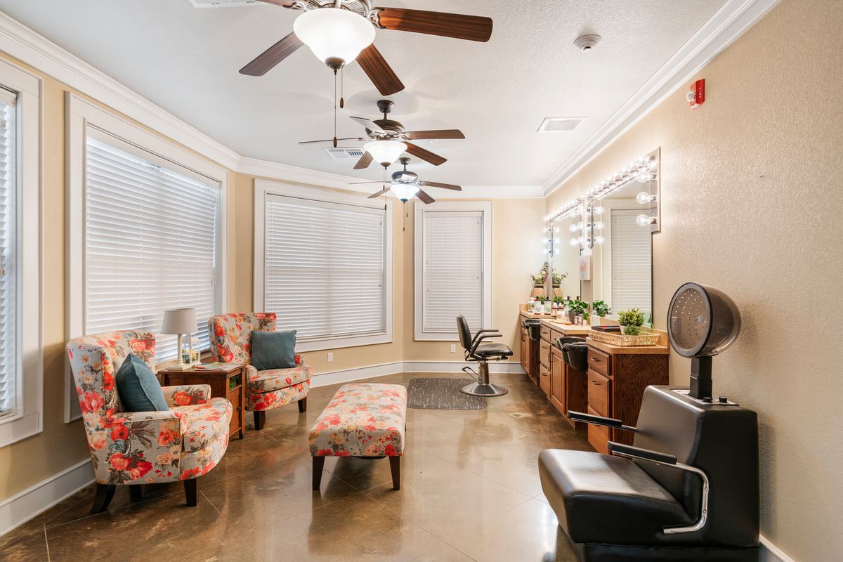 A well-lit salon interior with comfortable seating, multiple mirrors, and ceiling fans.