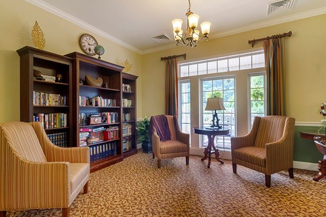 A cozy library room with bookshelves, armchairs, and large windows.