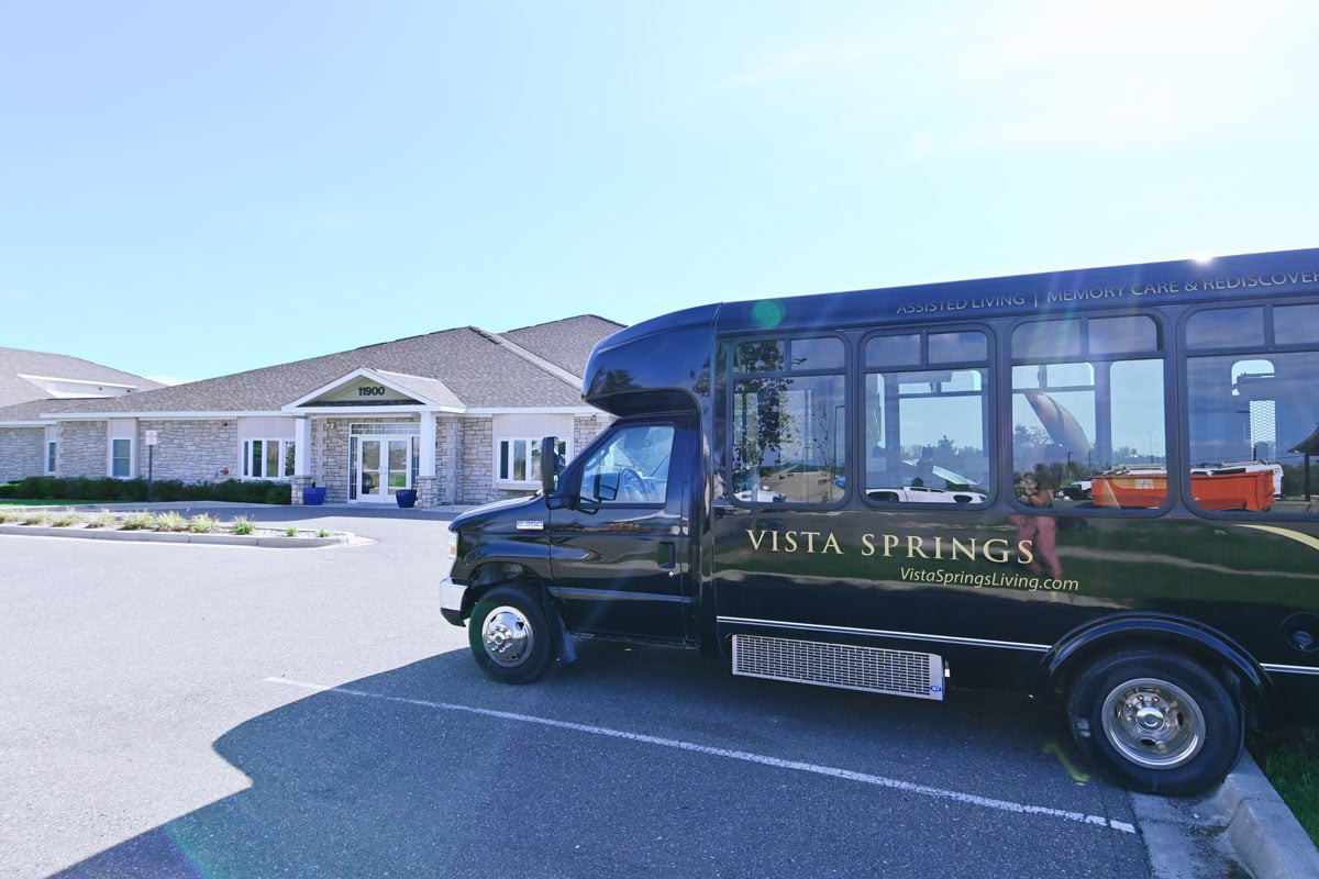 A black shuttle bus parked in front of a building on a sunny day.