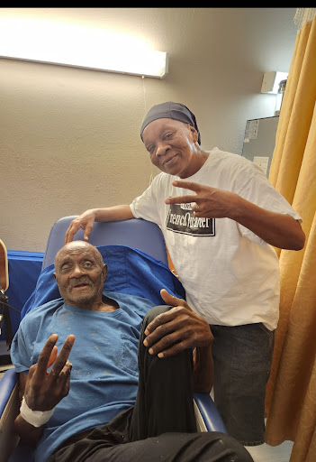 Two friends sharing a moment in a hospital setting, both smiling and making peace signs.