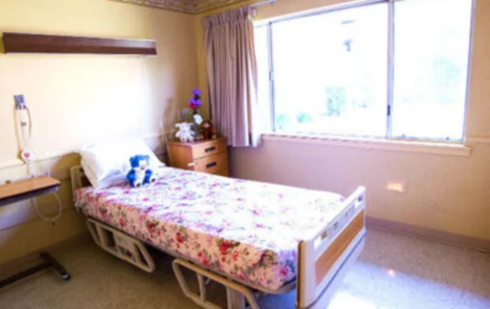 A bright room with a hospital bed, floral bedspread, and large window.
