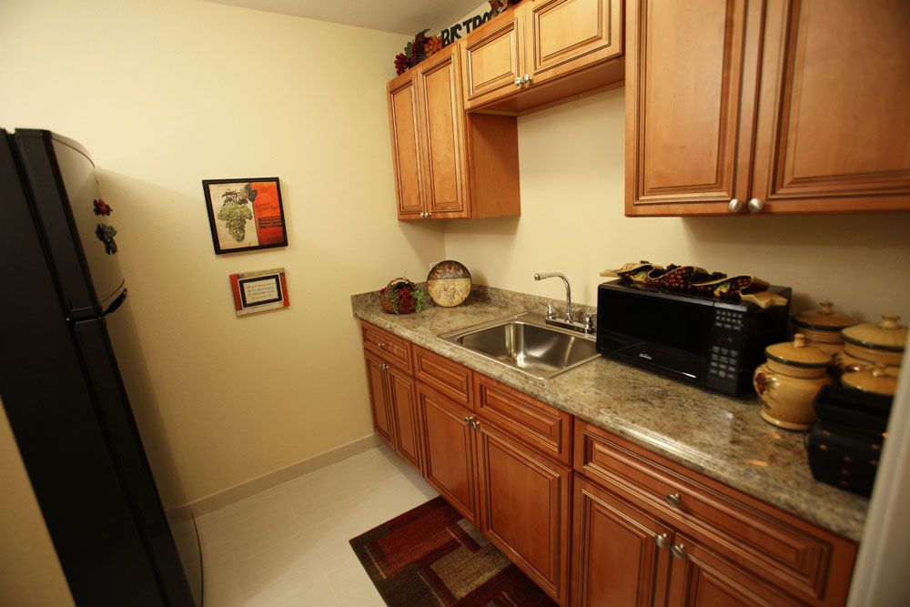 A compact kitchen with wooden cabinets, a countertop sink, and a microwave.