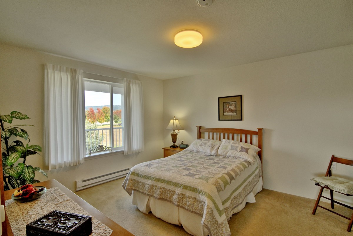 A cozy bedroom with a neatly made bed, lamp, and window view.