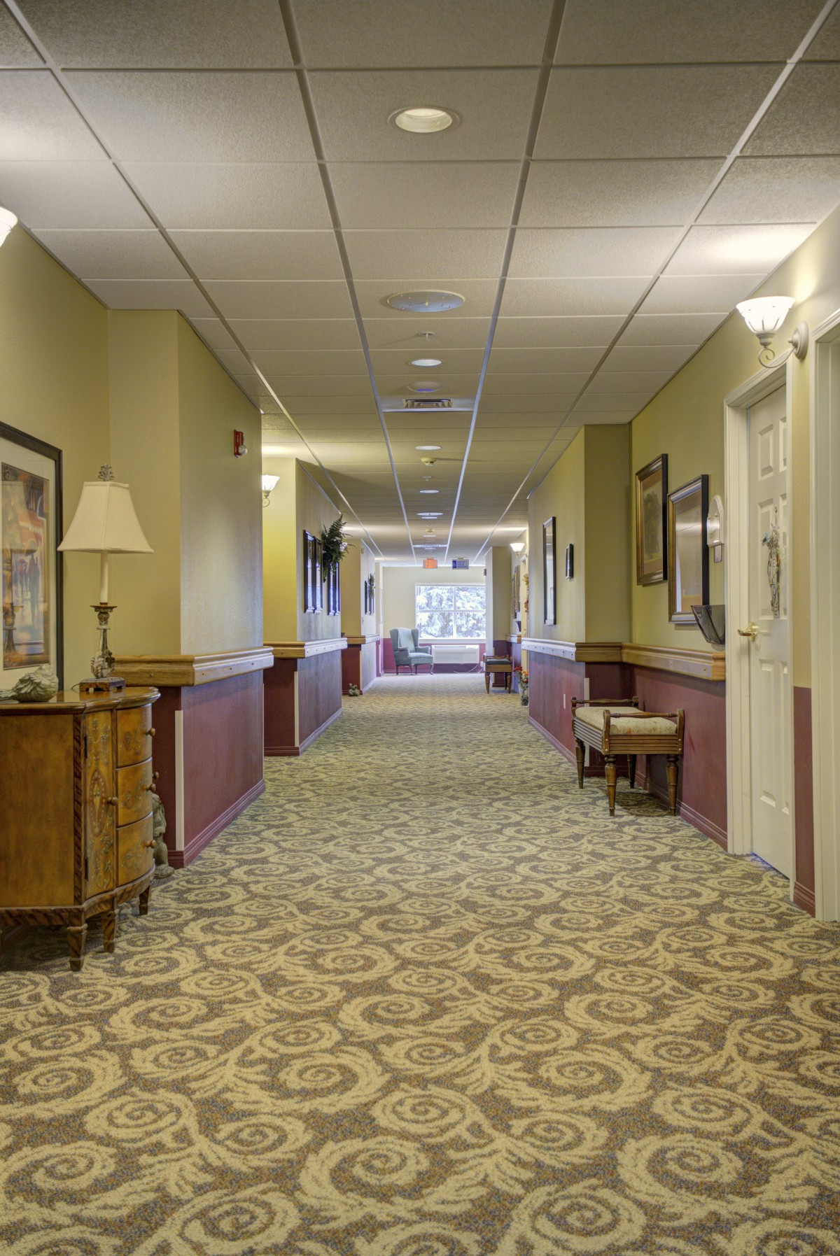 A well-lit hallway with carpeted flooring and decorative furniture.