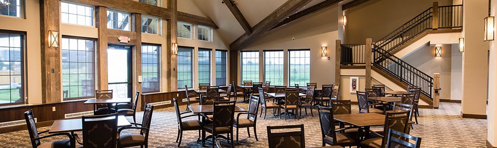 An empty dining room with tables and chairs, featuring large windows and a vaulted ceiling.