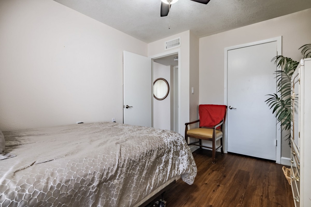 A simple bedroom with a bed, chair, and doors, featuring wooden flooring and white walls.