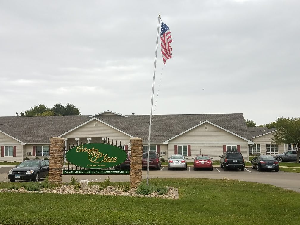 A building with an American flag and signage at the entrance, surrounded by parked cars.
