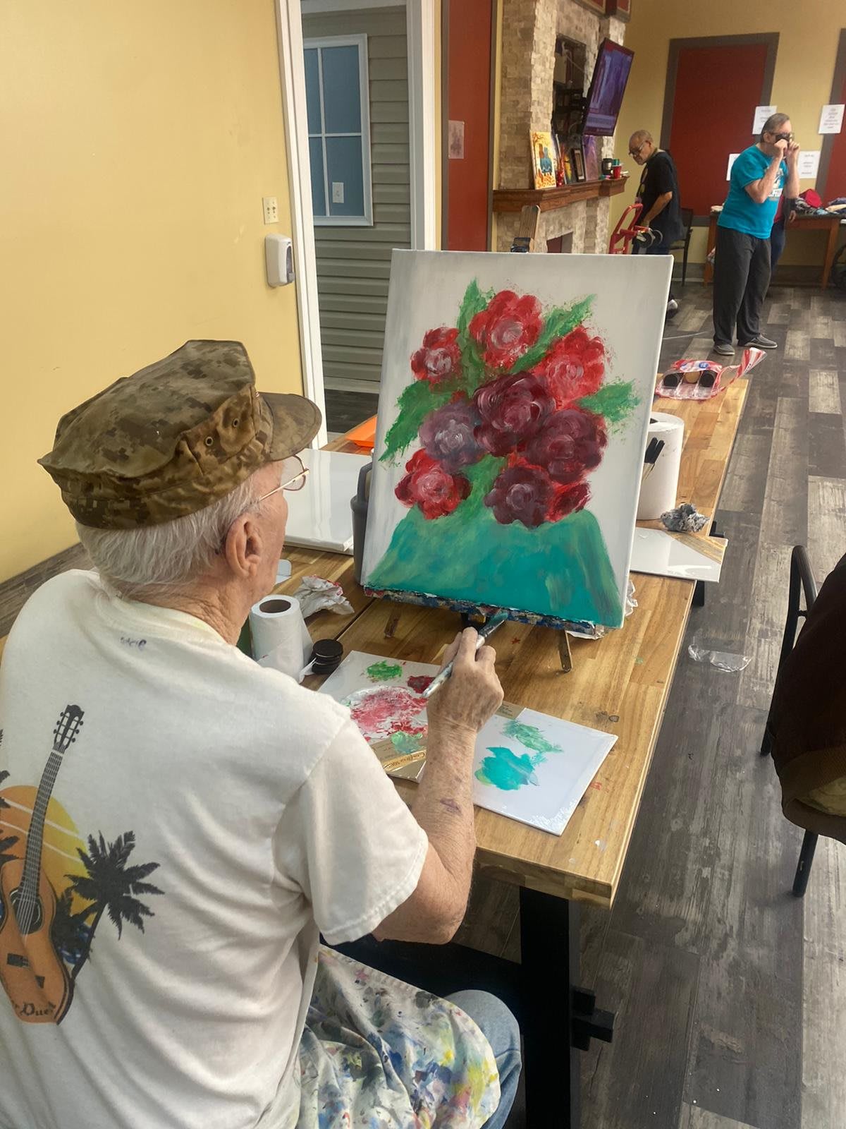 An artist painting a vibrant bouquet of flowers on an easel indoors.