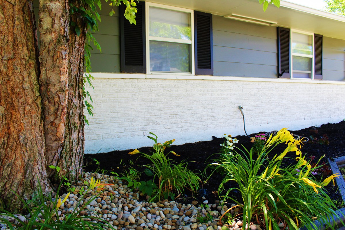A neatly landscaped garden area with various plants and a stone border in front of a house.