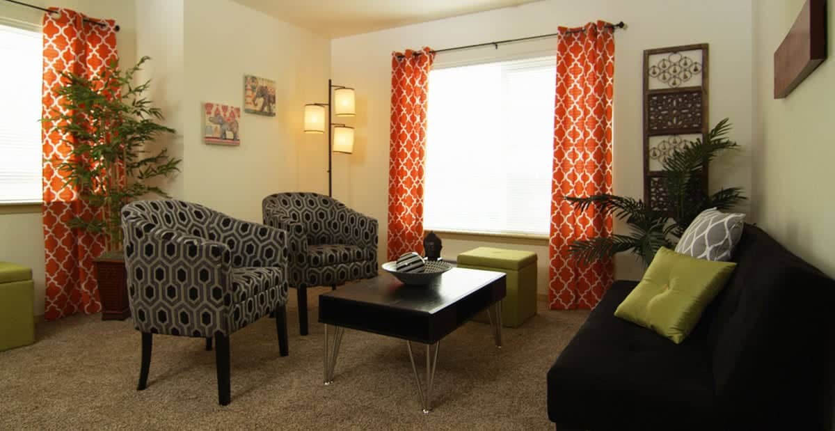 A modern living room with patterned curtains, stylish armchairs, and a sleek black coffee table.