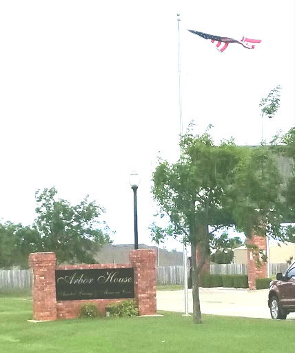 An entrance sign with a flag flying above it, surrounded by greenery.