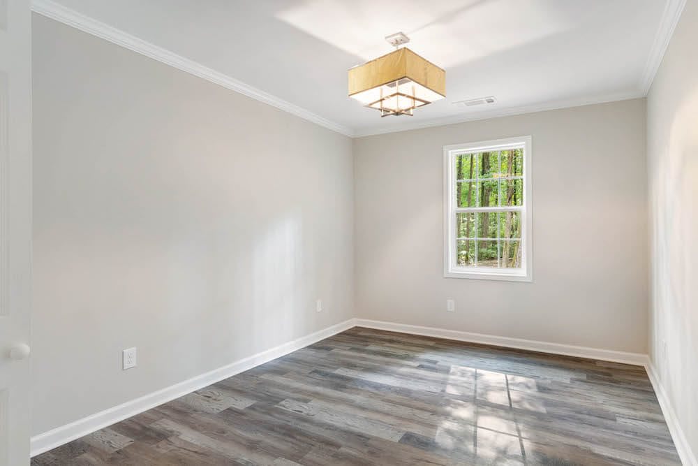 A bright, empty room with hardwood floors and a modern light fixture.