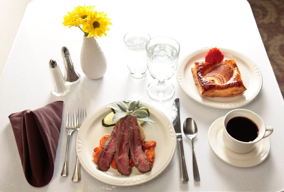 A breakfast table setting with bacon, a pastry, coffee, and yellow flowers.