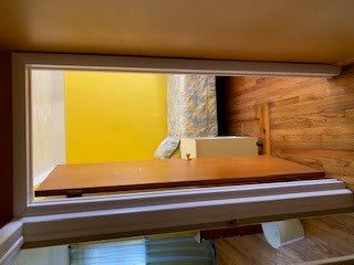 A view through an open doorway into a bedroom with a yellow wall and wooden flooring.