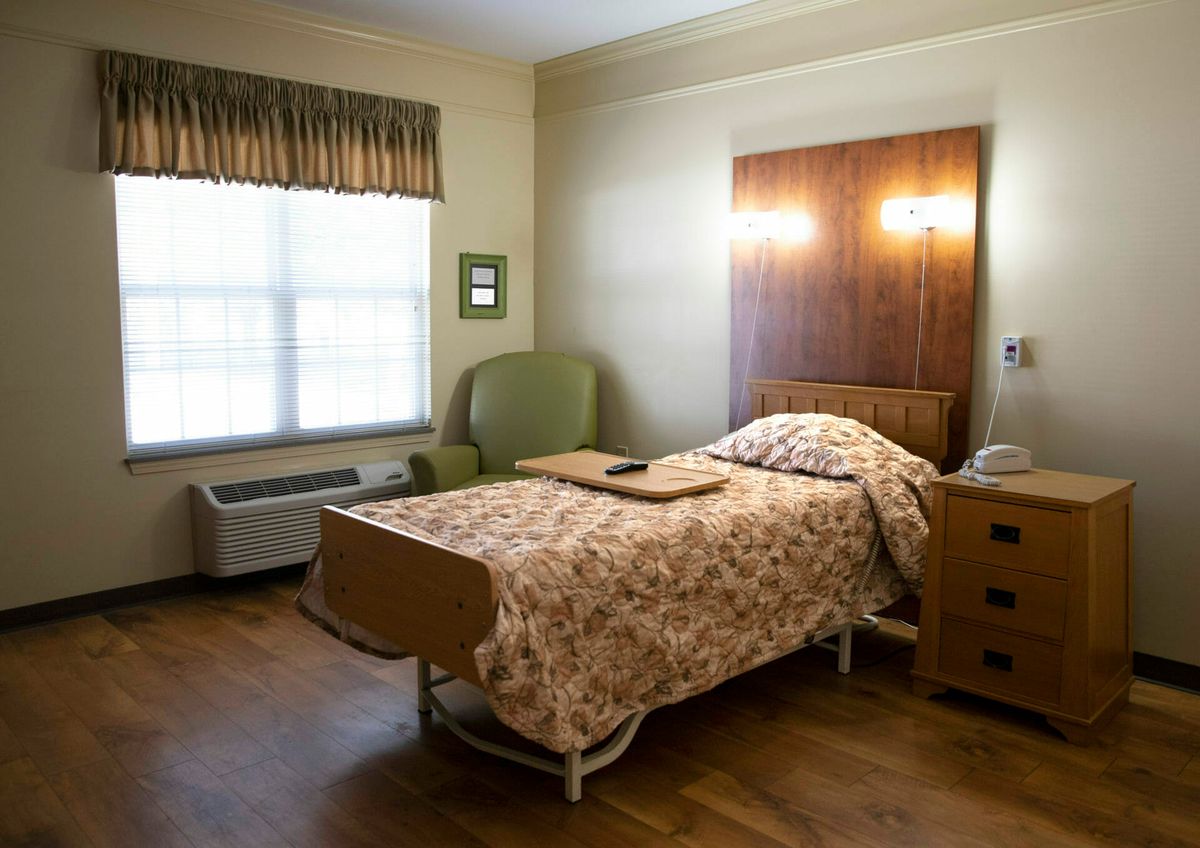 A hospital room with a single bed, chair, and window.