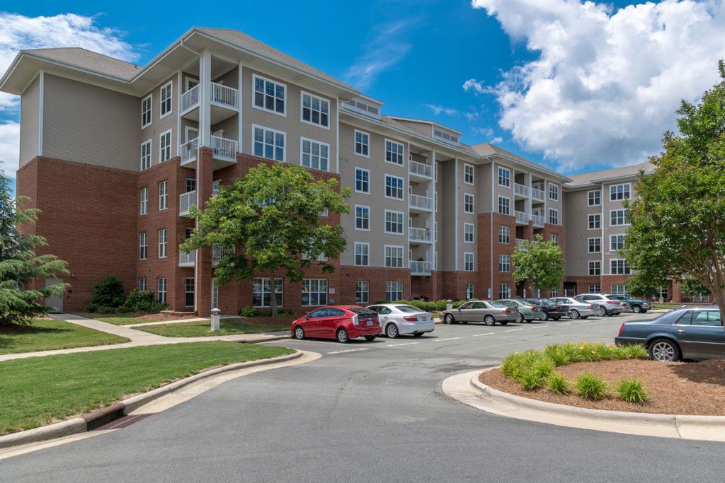 A modern multi-story apartment building with a parking lot and landscaped surroundings.
