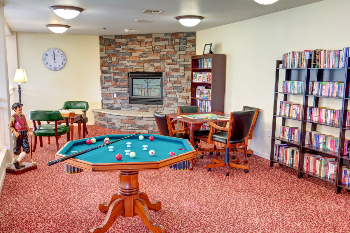 A cozy game room featuring a pool table, bookshelves, and a fireplace.