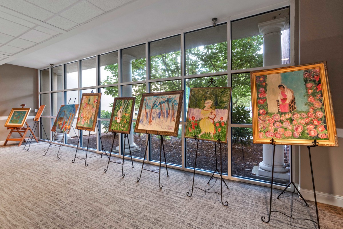 A row of paintings displayed on easels in a well-lit gallery space.