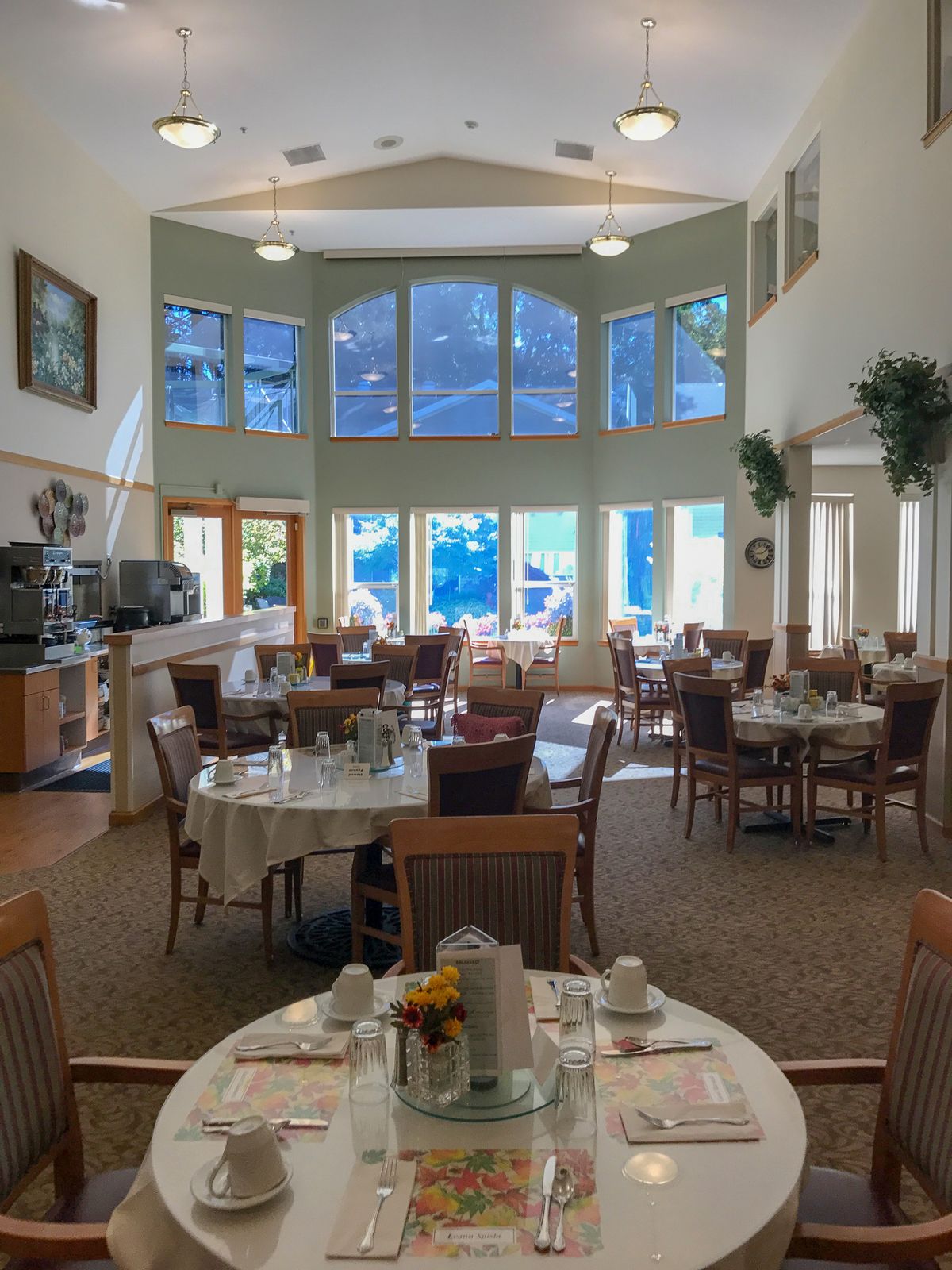 A spacious dining area with large windows letting in natural light, featuring neatly arranged tables and chairs.