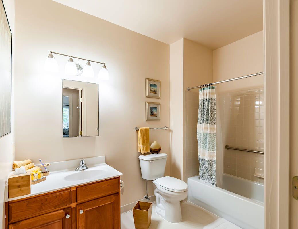 A well-lit bathroom with a vanity, mirror, toilet, and a bathtub with a shower curtain.