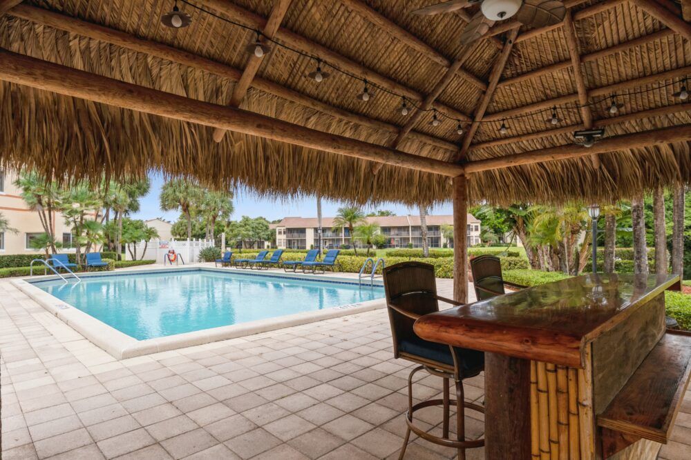 A tranquil outdoor setting featuring a tiki hut with seating, overlooking a swimming pool surrounded by lush greenery.
