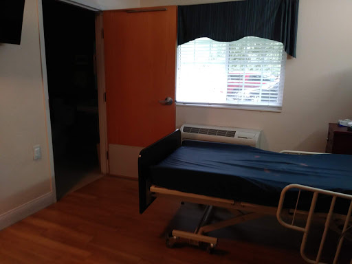 A hospital room featuring a bed, window, and wooden flooring.