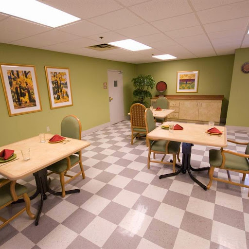 A cozy dining area featuring simple tables and chairs against a green backdrop, complemented by decorative artwork.