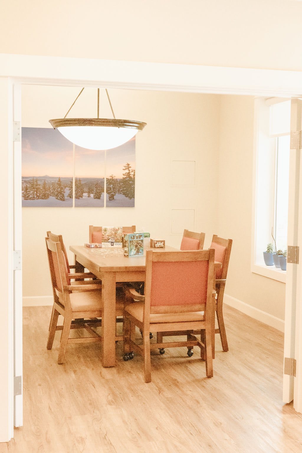A cozy dining room with a wooden table and chairs, illuminated by a central chandelier.