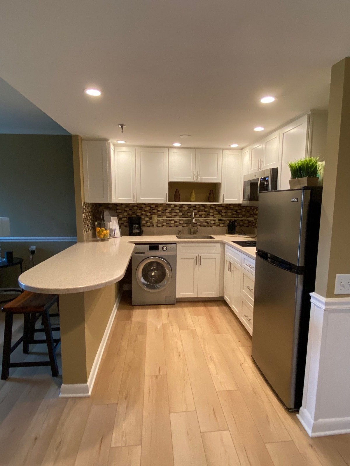 A modern kitchen featuring white cabinets, a refrigerator, and a washing machine with wooden flooring.