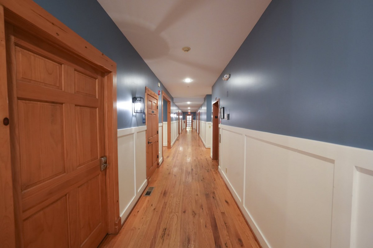 A long hallway with wooden floors and blue walls, lined with doors on either side.