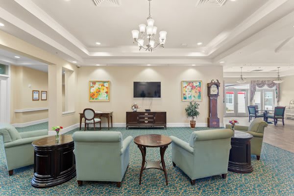A cozy living room with comfortable armchairs, a central table, a flat-screen TV, and decorative artwork on the walls.