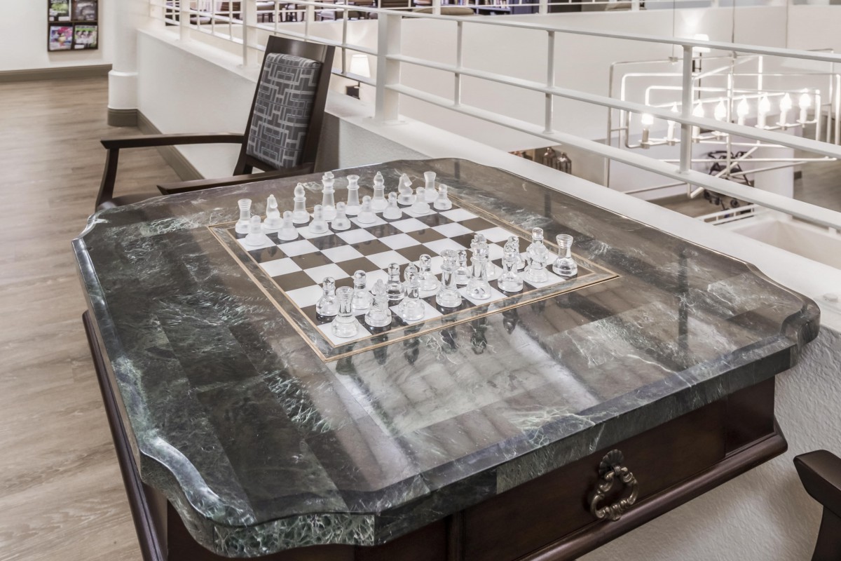 A glass chessboard set up on an elegant wooden table in a modern interior space.