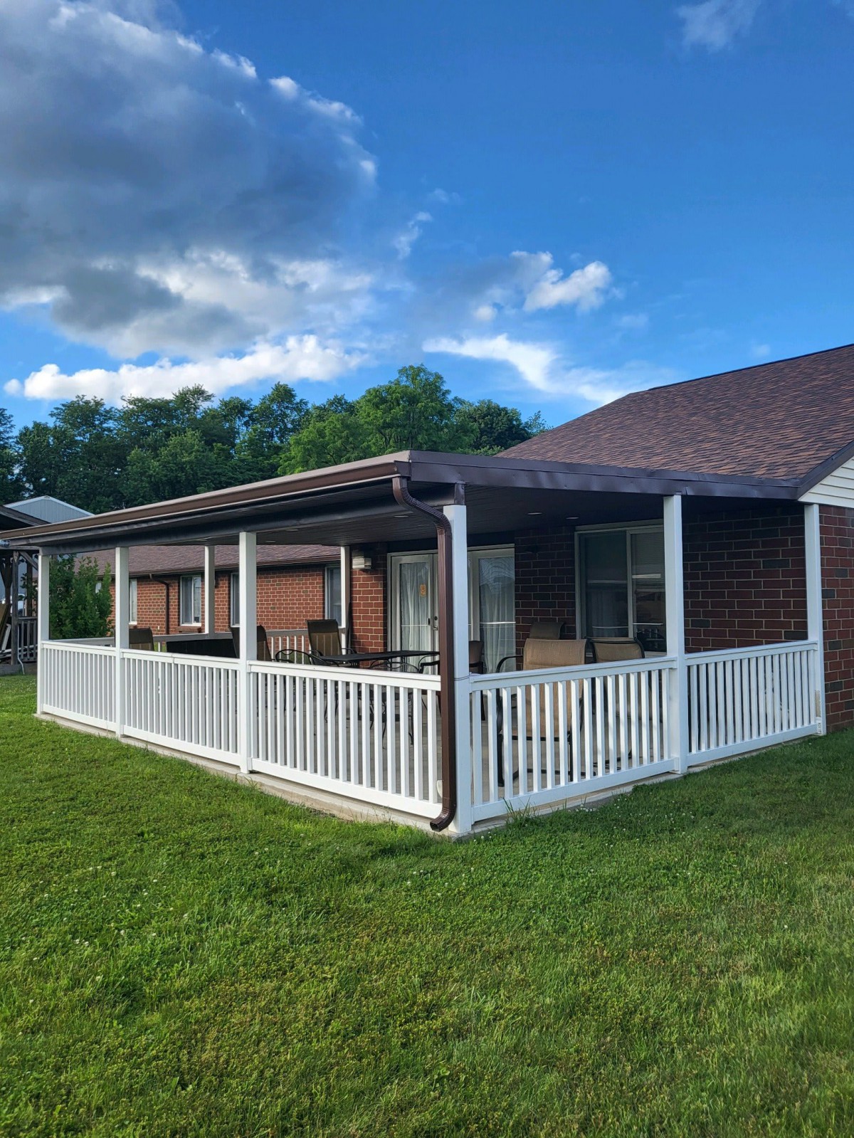 A house with a covered porch and white fence set against a backdrop of trees and a blue sky.