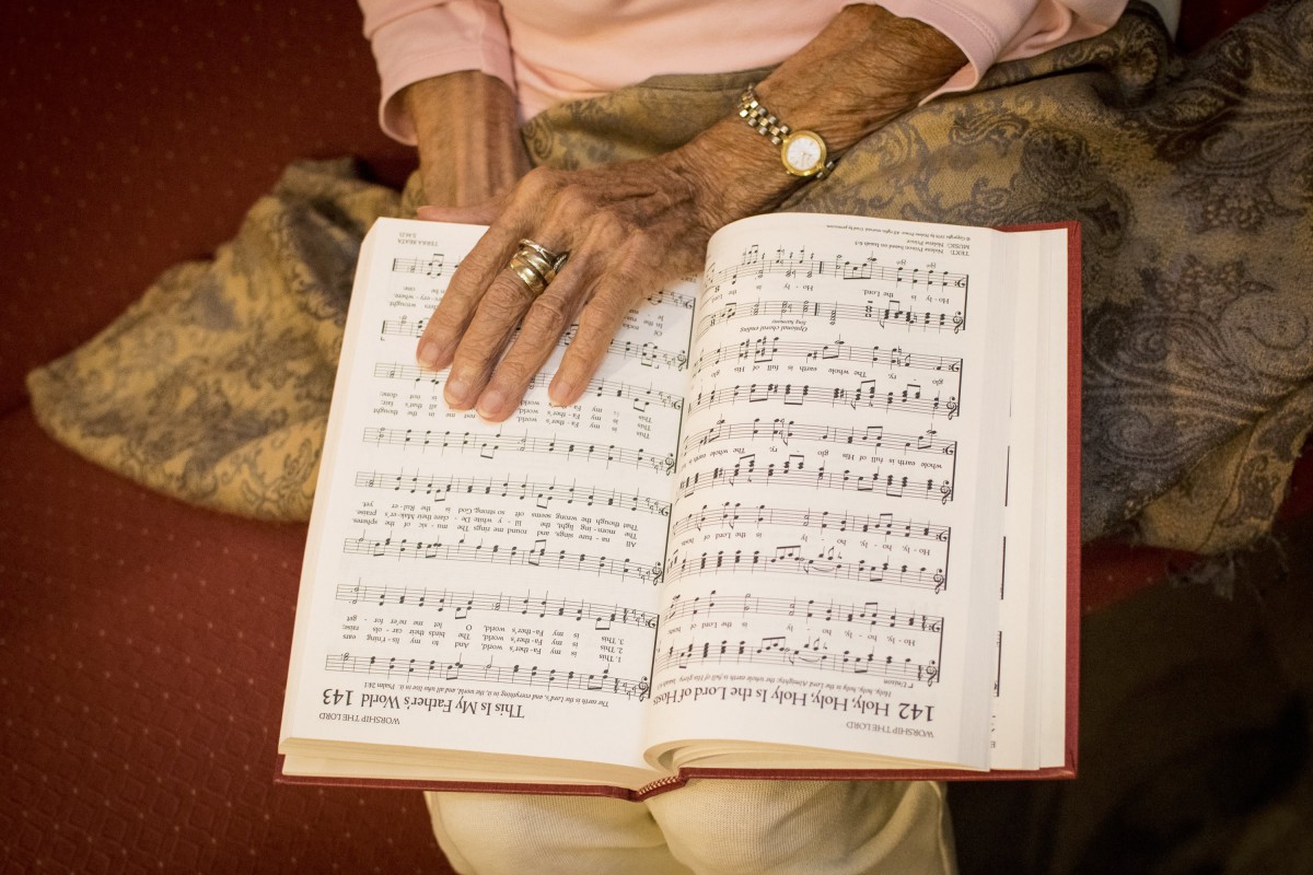 An elderly person reading from a sheet music book.
