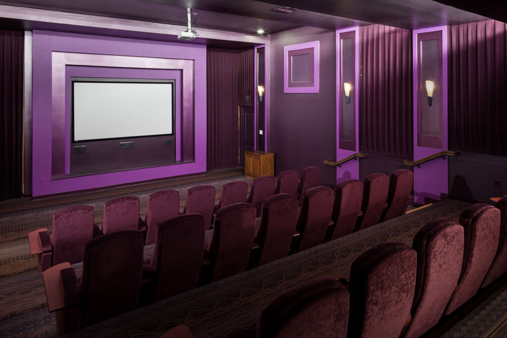 A cozy cinema room with purple lighting and rows of comfortable seating facing a large screen.