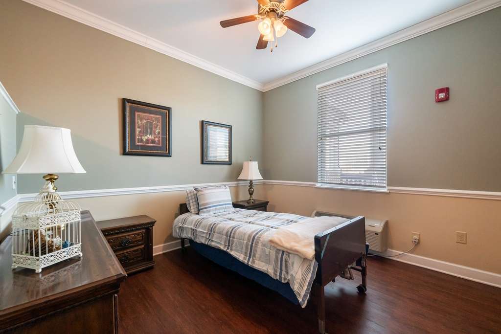 A cozy bedroom with a single bed, wooden furniture, and a ceiling fan.