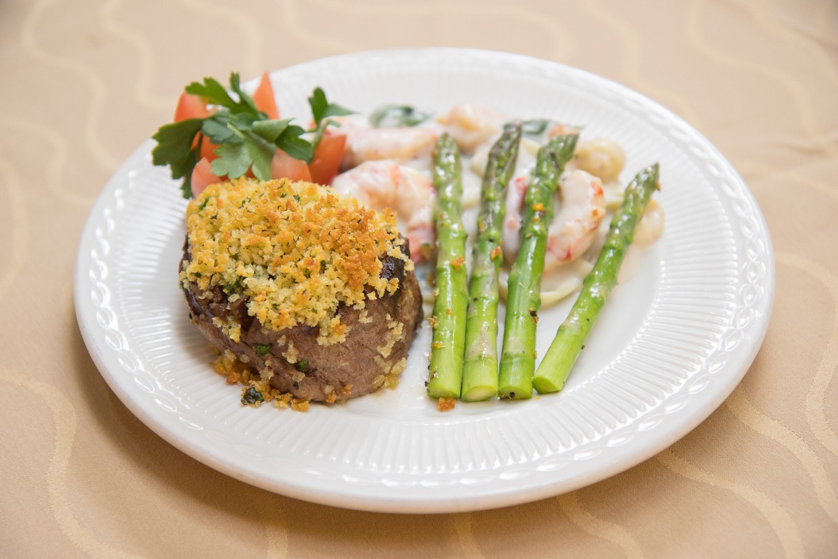 A plated dish featuring crusted steak, asparagus, and a side of creamy chicken with garnish.