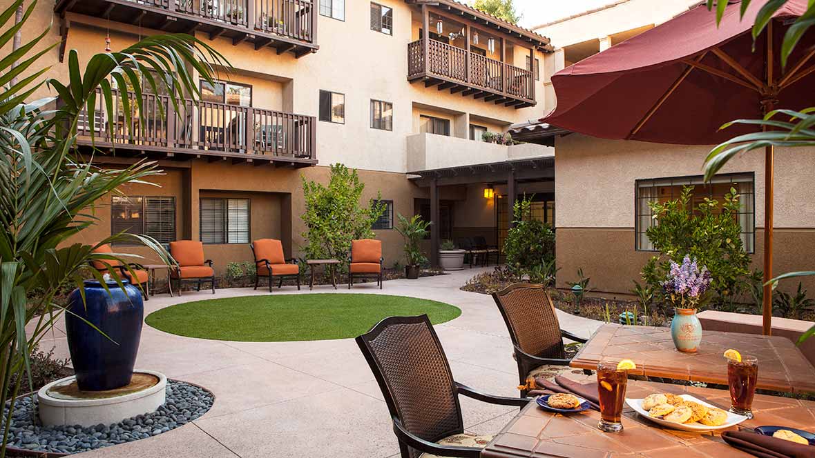 A cozy courtyard with outdoor seating and lush plants surrounded by a multi-story building.