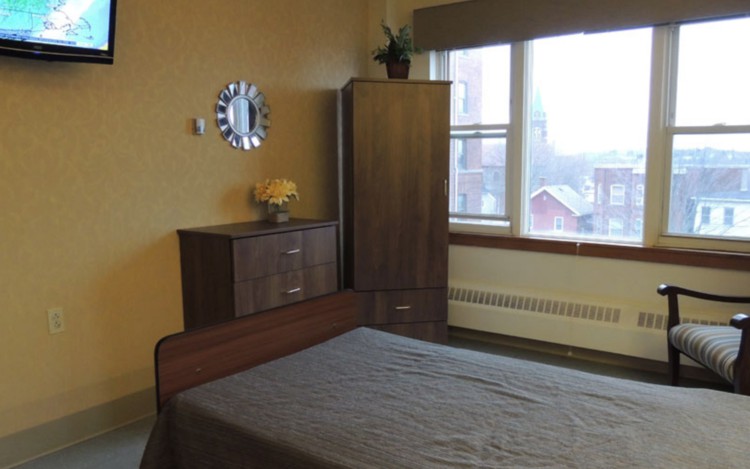 A simple bedroom with a bed, wardrobe, chest of drawers, and a window.