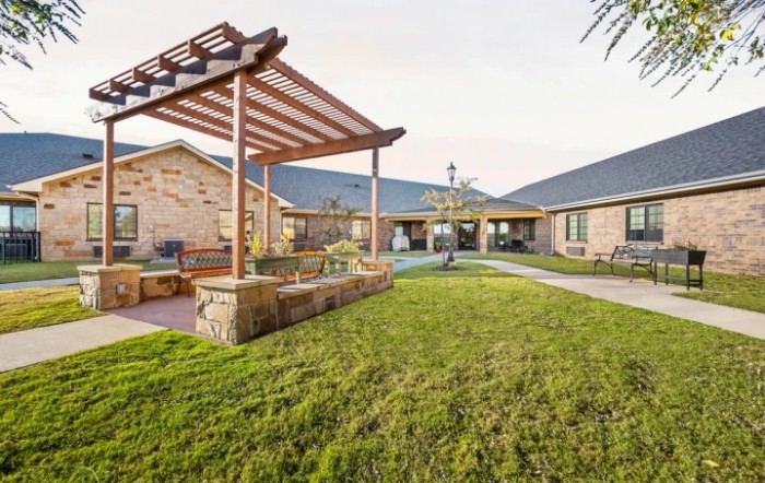 A beautifully landscaped garden featuring a wooden pergola and a well-maintained lawn in the courtyard of a brick building.