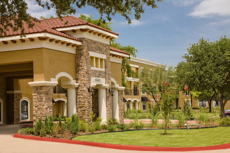 A sunny day view of a beautiful building with stone and stucco architecture surrounded by trees and grass.