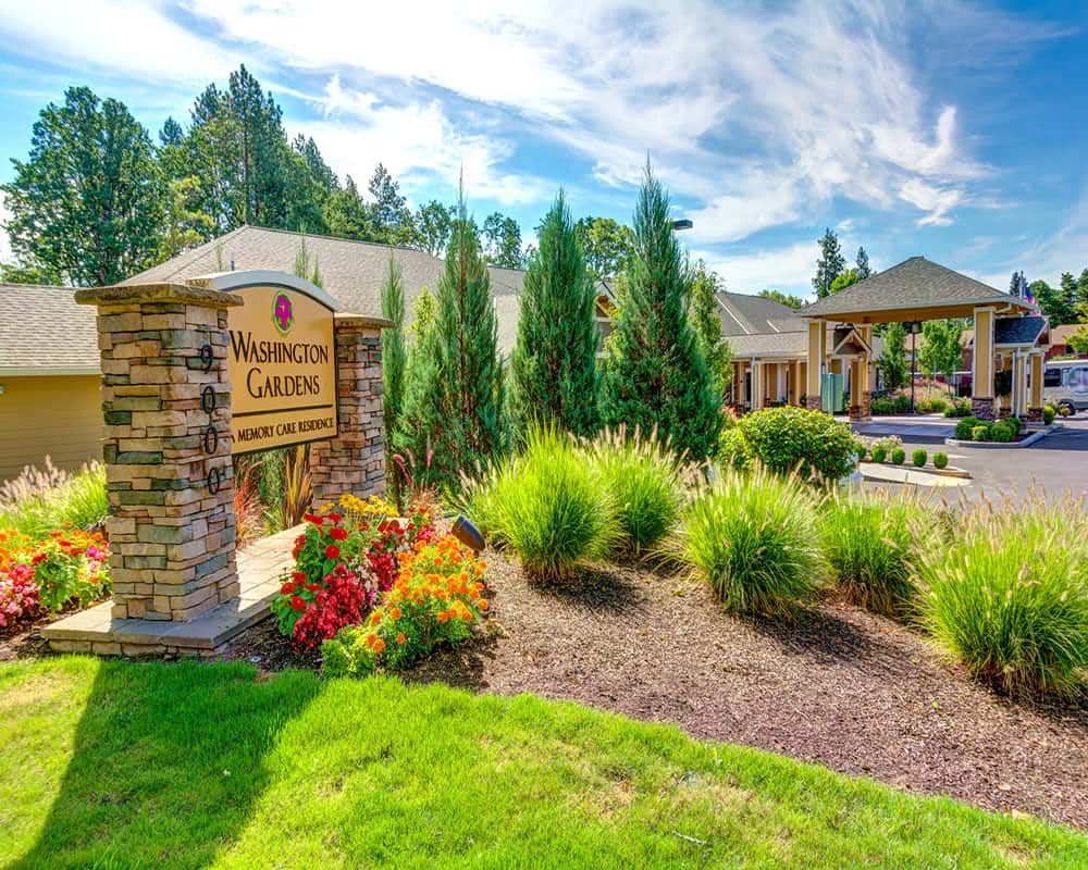 A beautiful landscaped garden with a stone sign and neatly manicured grounds in front of a building.