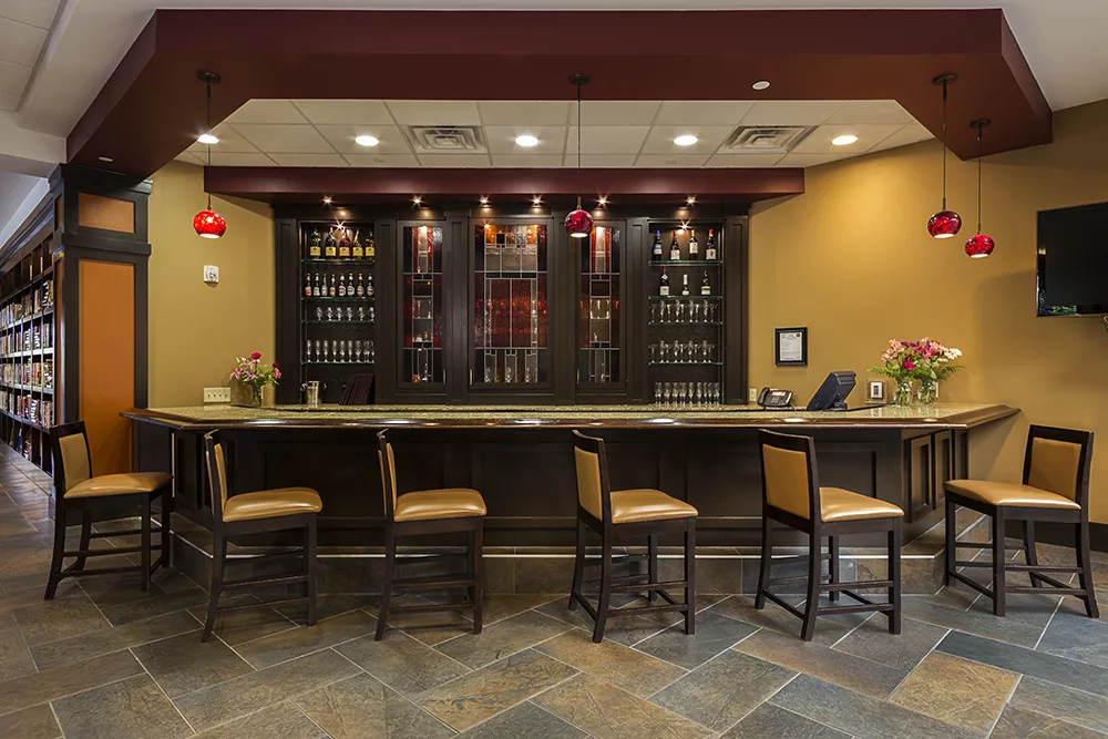 A cozy bar interior with a counter and stools, featuring an array of wines on display.