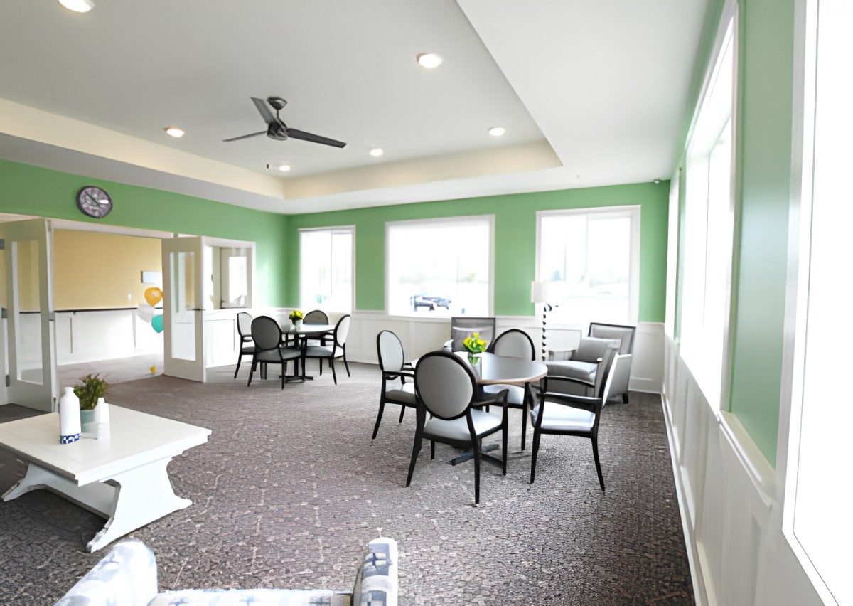 A bright and modern dining area with green walls, featuring multiple tables and chairs under natural lighting.