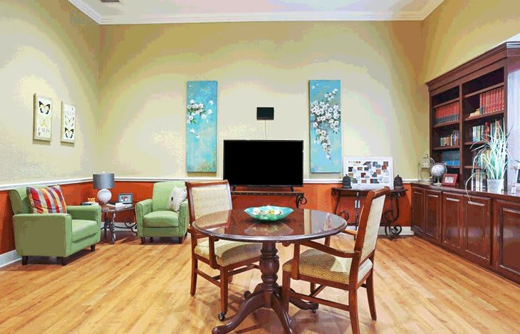 A cozy living room with a round wooden table, chairs, and a large television surrounded by colorful artwork.
